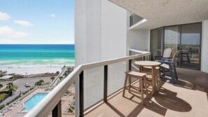 Ein Balkon mit Blick auf Strand und Meer, ein Pool sowie ein Tisch mit Stühlen.