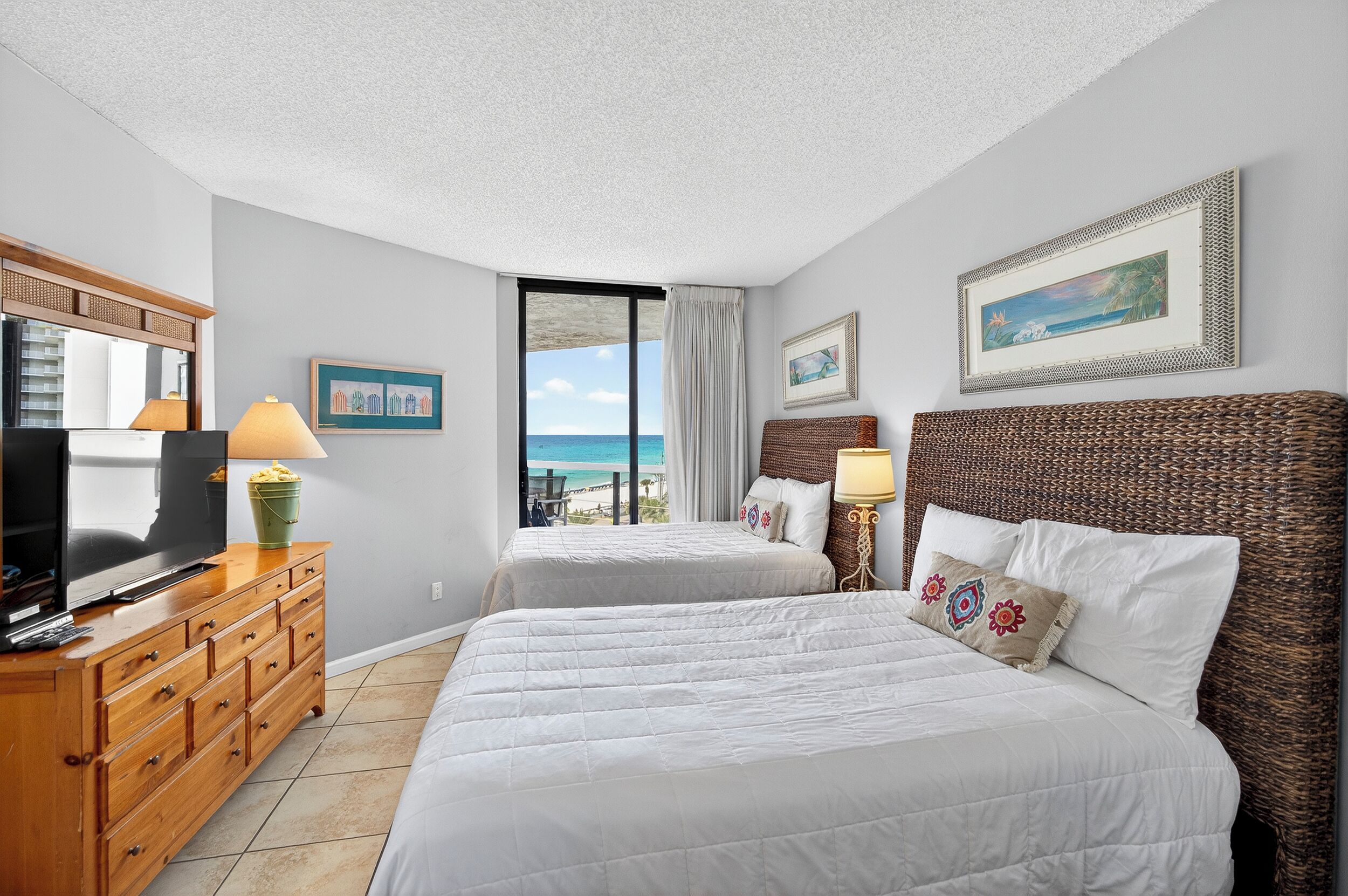 A hotel room with two beds, a television, a dresser, and a view of the ocean.