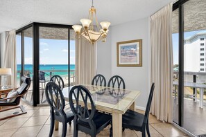 A dining area with a glass table, black chairs, a chandelier, a framed picture, and a view of the ocean. - Free Beach SRVC!! Free Beach Bonfires! Direct Ocean Views! Pickle Ball Courts (Miramar Beach)