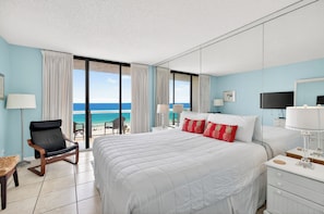 Habitación de hotel con una cama grande, una silla, un escritorio y vista al océano.