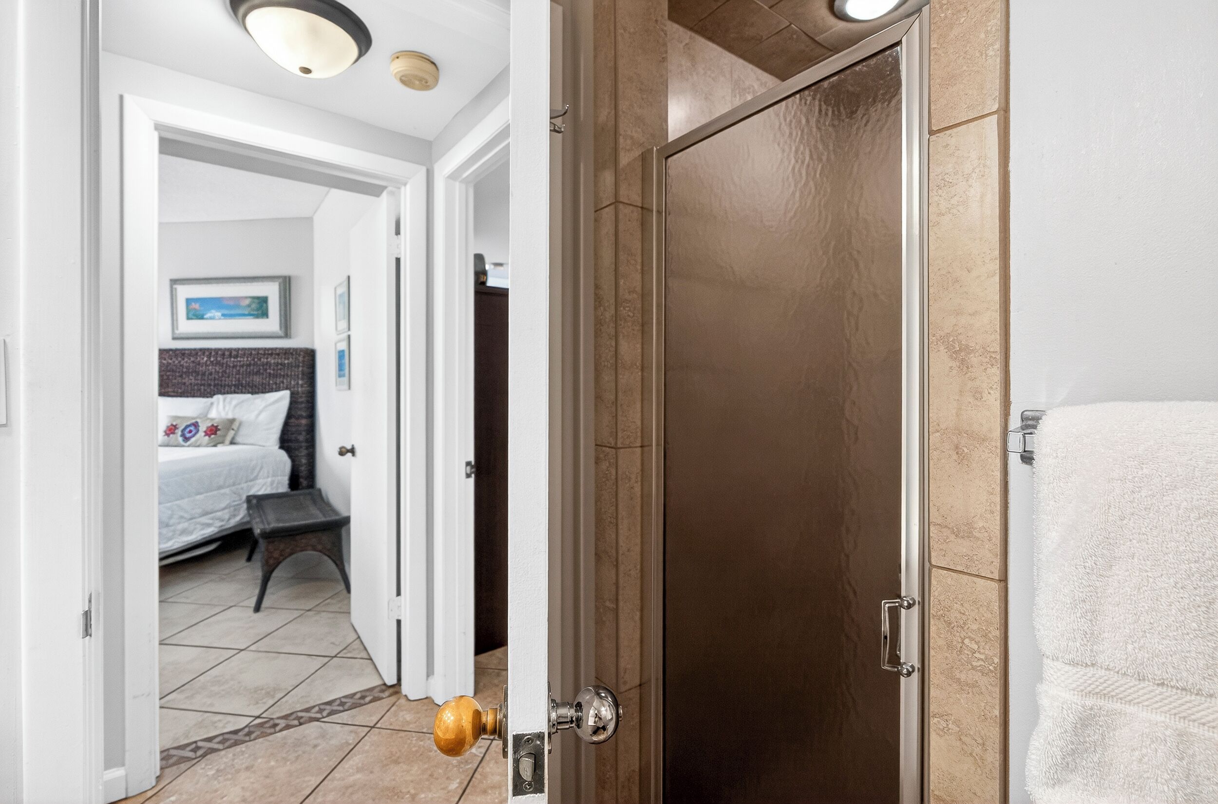 Una habitación de hotel con cama, mesita de noche y puerta que da a un baño con toalla.
