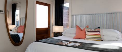 A bedroom with a large bed, a wooden door, a mirror, and a window with curtains.