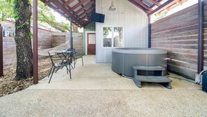 An outdoor patio area with a hot tub, a table with chairs, and a covered seating area. - Unique Limestone Pumphouse + Private Hot Tub (Fredericksburg)