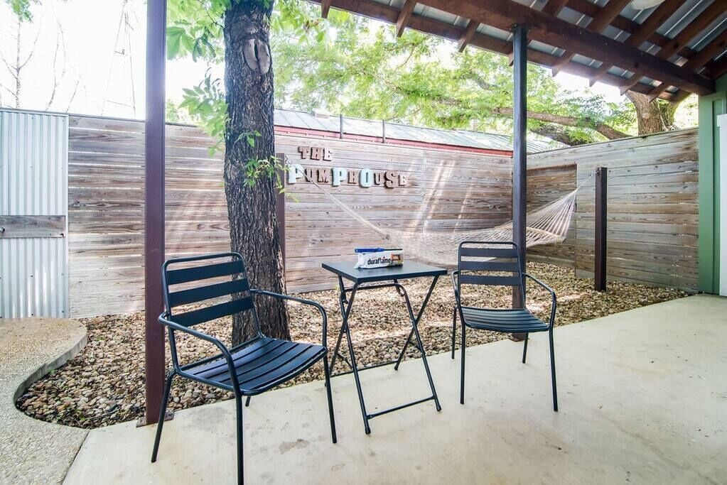 Un patio abrité avec deux chaises en métal, une petite table et un hamac. Un mur en bois sur lequel on peut lire l’inscription « THE PILPHOUSE » est visible à l’arrière-plan.