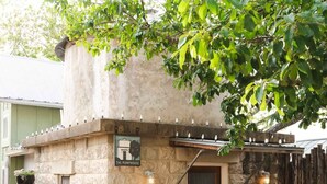 A stone building with a sign reading 'The Pumphouse,' a door, and a small porch area. - Unique Limestone Pumphouse + Private Hot Tub (Fredericksburg)