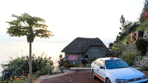 A stone building with a thatched roof, a welcoming sign, and a parked car in front. - Hakuna Matata Lodge (Gisenyi)
