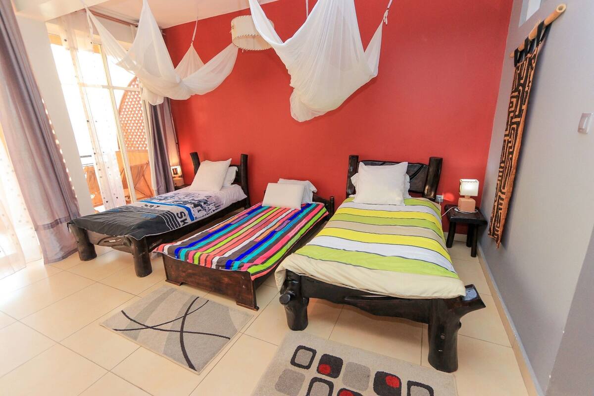 Quarto com duas camas, parede vermelha e uma janela grande com cortinas.