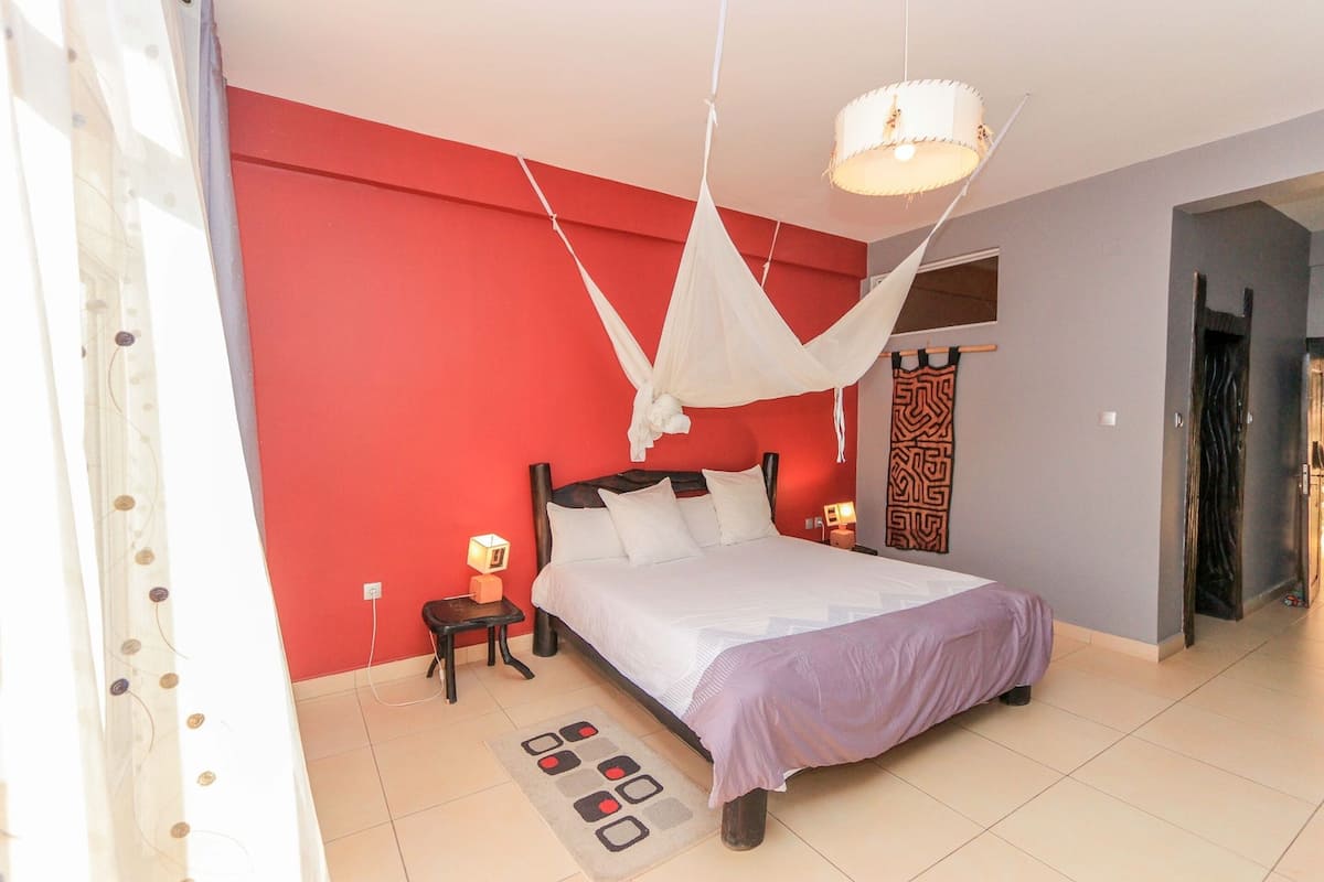Quarto com cama, mesa de cabeceira, luminária, dossel pendurado e tapete estampado.