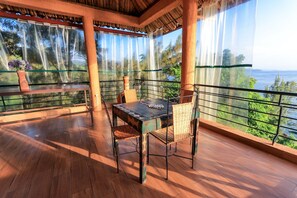 Una terraza de madera con una mesa, sillas, una planta en maceta y vistas al mar.