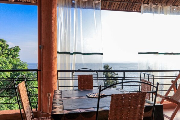 Un balcón con mesa y sillas, que ofrece vistas panorámicas del océano y la vegetación.