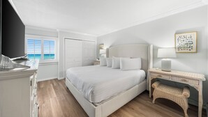 Um quarto com uma cama grande, uma mesa de cabeceira, uma luminária e vista para o mar através de uma janela.
