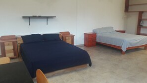 A bedroom with a large bed, a smaller bed, two nightstands, a wooden chair, and a desk.