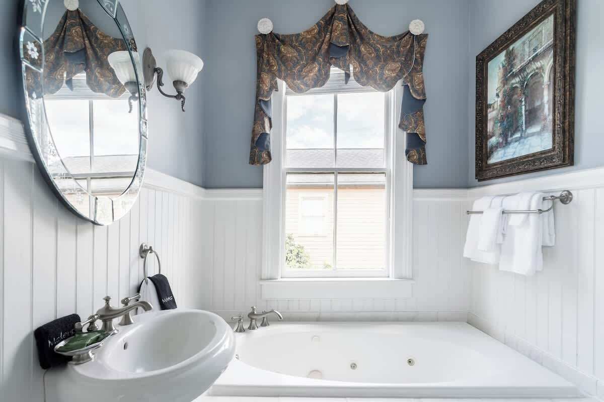 Une salle de bain avec un grand miroir, un lavabo, une baignoire et une fenêtre avec des rideaux.