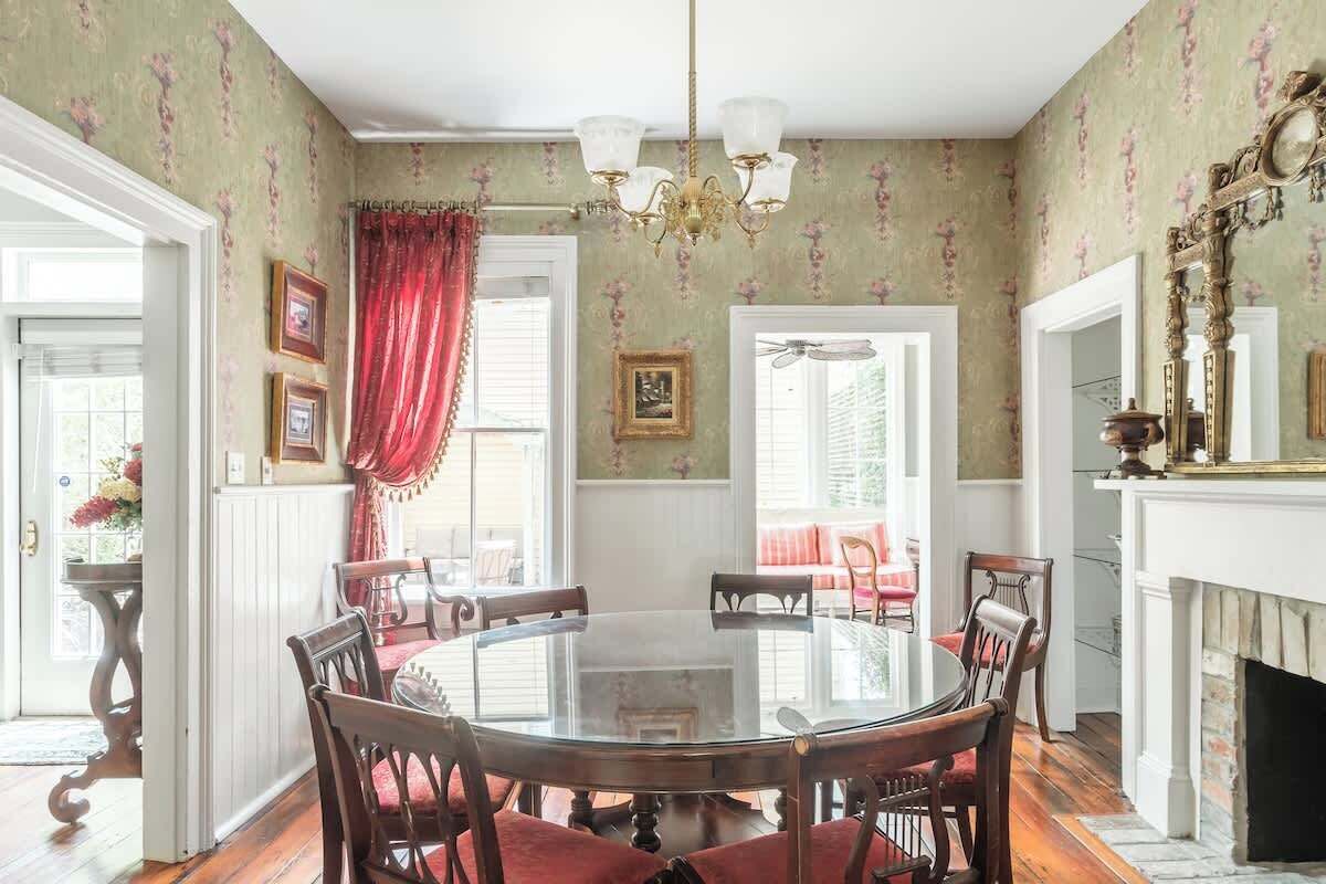 Une salle à manger avec une table ronde en verre, entourée de chaises en bois, un lustre et une cheminée.