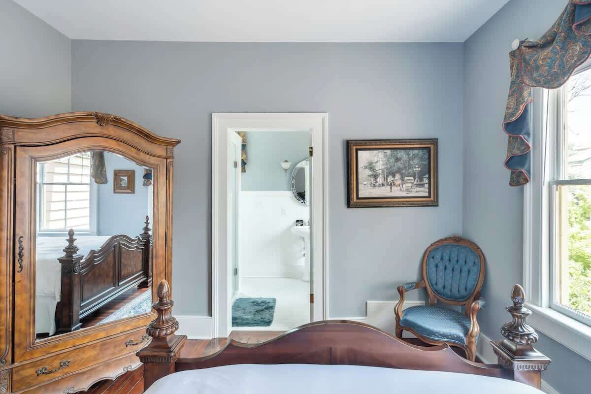 Un dormitorio con un amplio aparador de madera, una silla, una cama y un cuadro en la pared.