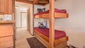 Habitación con literas, vigas de madera, un escritorio con silla y una puerta al fondo.