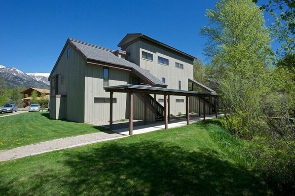 A two-story building with a covered outdoor area and a mountain backdrop. - JHRL - Geranium 2612 - First floor Aspens condo (Wilson)