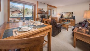 Un comedor con una mesa de madera dispuesta para dos, una chimenea y un televisor.