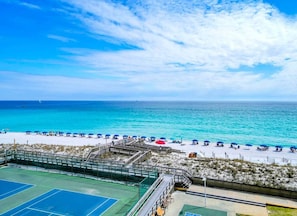 A beach with a tennis court, beach umbrellas, and a clear view of the ocean.