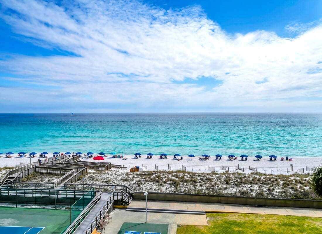 A beach view with a tennis court, beach umbrellas, and a wooden walkway.