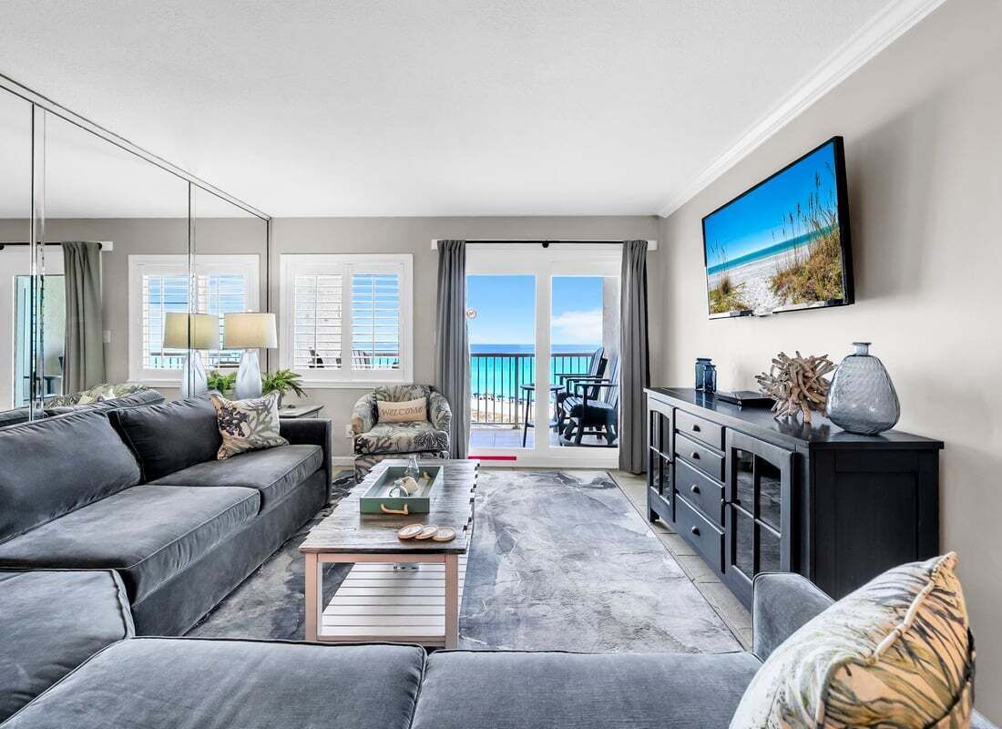 A modern living room with a grey sofa, a coffee table, a TV, and a balcony with a view.