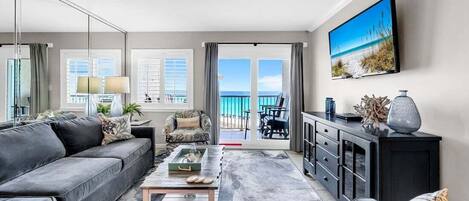 A modern living room with a grey sofa, a coffee table, a TV, and a balcony with a view.