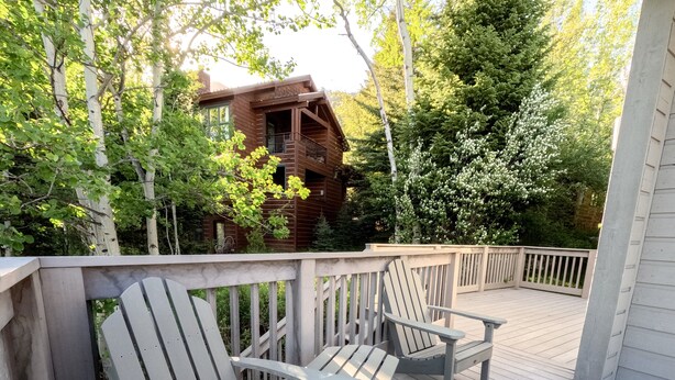 A wooden deck with Adirondack chairs and a view of a rustic cabin surrounded by trees. - JHRL - Uncle Al's Timber Ridge 1 townhome, steps from Moose Creek lift (Teton Village)