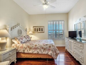 A bedroom with a bed, bedside tables, a dresser, a ceiling fan, a window with blinds, and artwork on the wall. - 304W ~ Relax with beautiful Gulf views in this 3BR/3BA center condo (Gulf Shores)