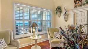 A room with a large window, wicker furniture, a small table with a lamp, and decorative wall art. - 304W ~ Relax with beautiful Gulf views in this 3BR/3BA center condo (Gulf Shores)