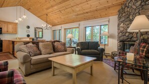 A cozy living room with a stone fireplace, wooden ceiling, and large windows. - JHRL - Teton Pines Townhome #21 (Wilson)