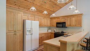 A kitchen with wooden cabinets, a white refrigerator, a black microwave, a stove, and pendant lights. - JHRL - Teton Pines Townhome #21 (Wilson)