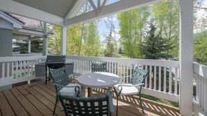 A covered patio with a round table and four chairs, a grill, and a white railing. - JHRL - Teton Pines Townhome #21 (Wilson)