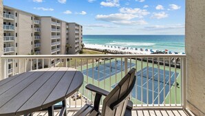 Een balkon met uitzicht op een strand en een tennisbaan.