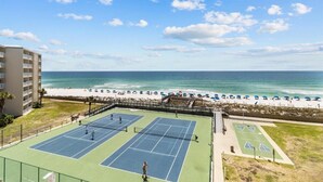 Een tennisbaan met twee velden, een strand en een gebouw op de achtergrond.