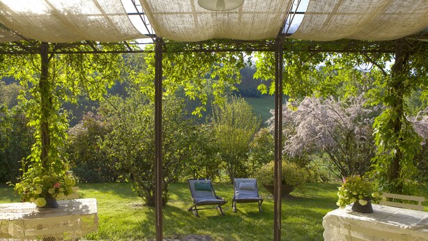 A covered outdoor seating area with two lounge chairs, a table with a lace tablecloth, and a potted plant. - Swimming pool villa with private chef on request (Salsomaggiore Terme, Parma)