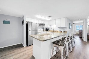 A modern kitchen with white cabinetry, stainless steel appliances, and a central island with bar stools.