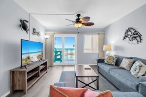 A living room with a television, a sofa, a coffee table, and a balcony with chairs. - 307- Coastal beachfront Charmer with direct GULF view and FREE beach service (Destin)