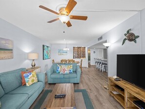 Uma sala de estar com ventilador de teto, televisão, sofá e um espaço de jantar com cadeiras e mesa.