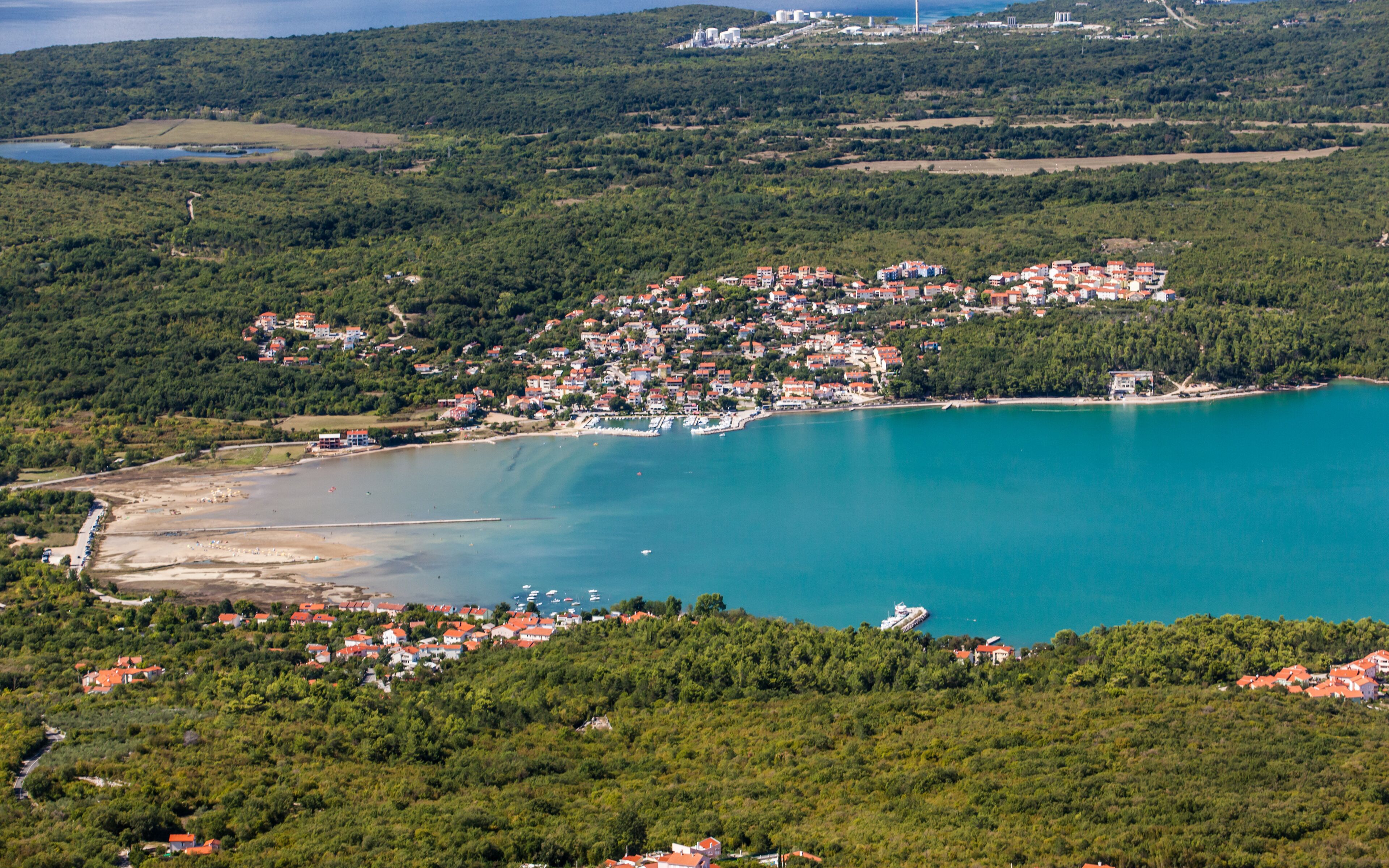Une ville côtière dotée d’un port de plaisance, entourée de collines et de verdure.