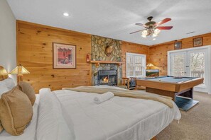 Quarto de madeira com cama, lareira, mesa de bilhar e ventilador de teto.