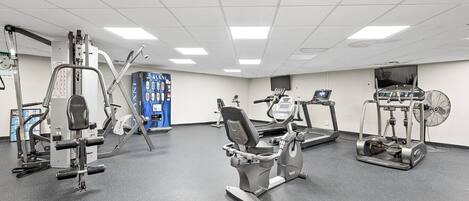 Une salle de sport équipée de divers appareils d’exercice, notamment un tapis de course, un vélo elliptique et des appareils de musculation.