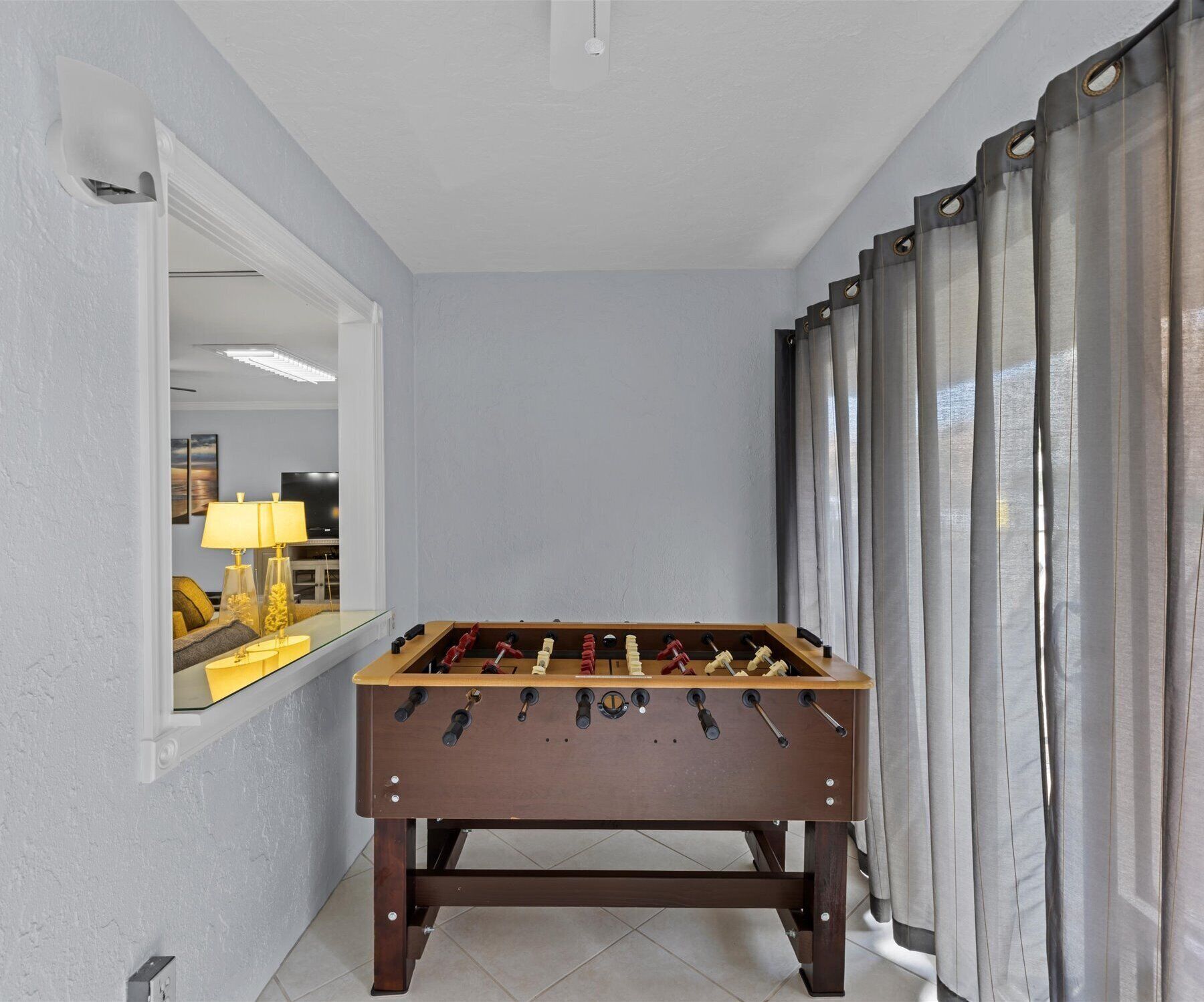 A room with a foosball table, a window with curtains, and a lamp.