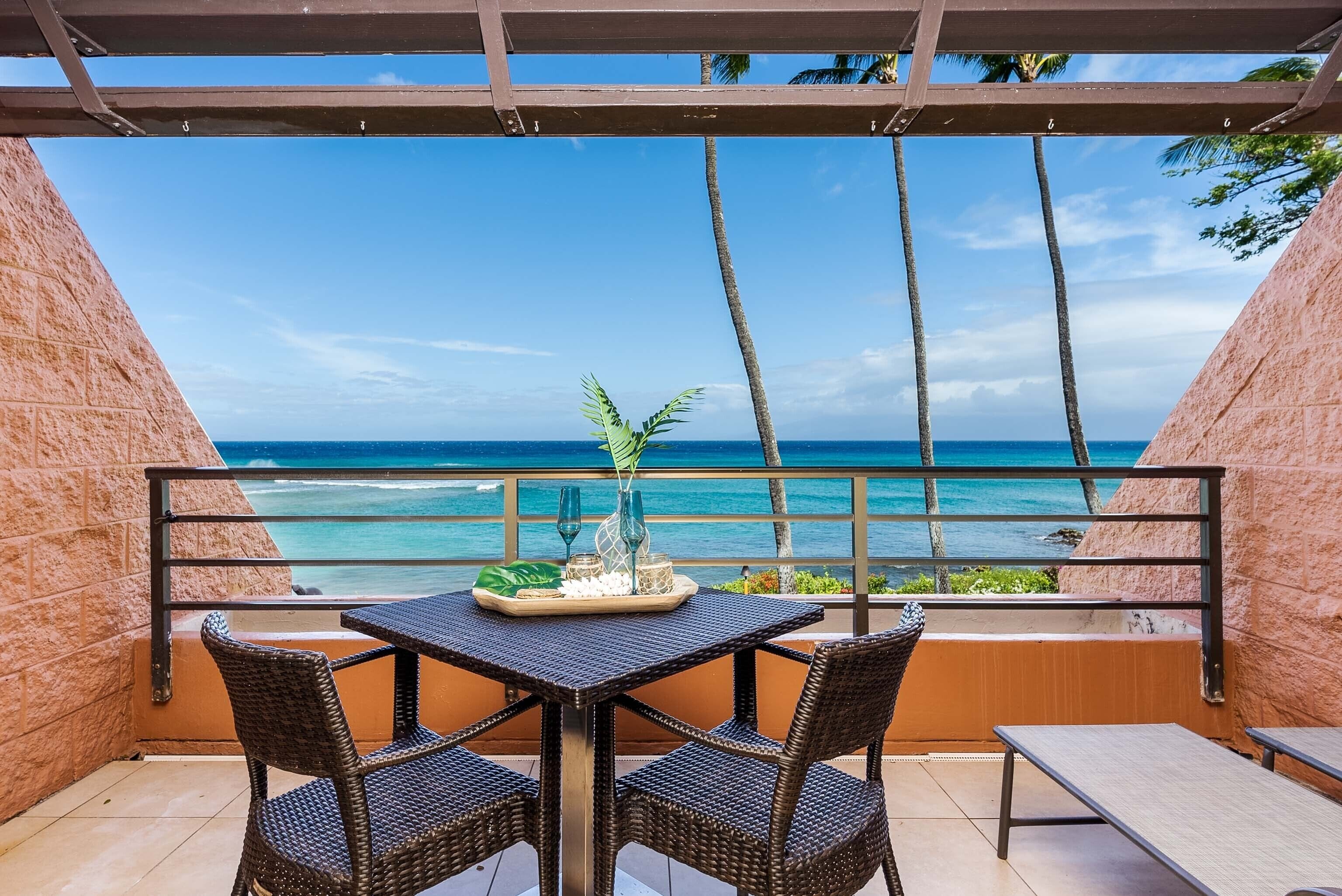 Ein Balkon mit Tisch und Stühlen mit Blick auf einen Strand, an dem Palmen und das Meer zu sehen sind.