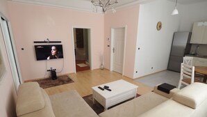 A modern living room with a beige sofa set, a white coffee table, and a flat-screen TV mounted on the wall. - New apartment in the city center (Praha)