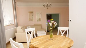 A dining area with a round wooden table, white chairs, a vase with flowers, and a beige sofa in the background. - New apartment in the city center (Praha)