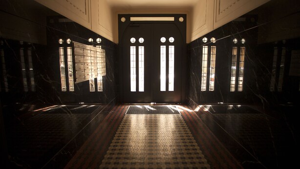 A hallway with a patterned floor, a central door with vertical windows, and walls with a dark, marble-like finish. - New apartment in the city center (Praha)