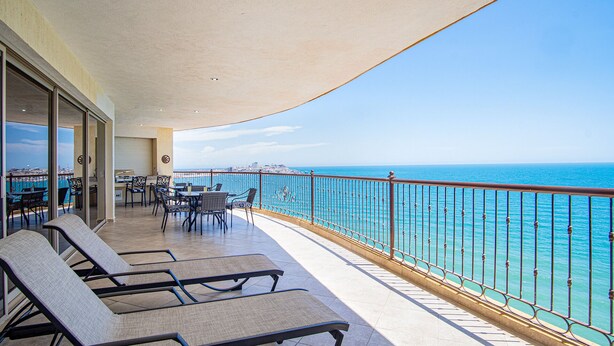 Een balkon met lounge fauteuils, een tafel en uitzicht op zee.