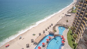Een resort met een groot zwembad, strand en uitzicht op zee.