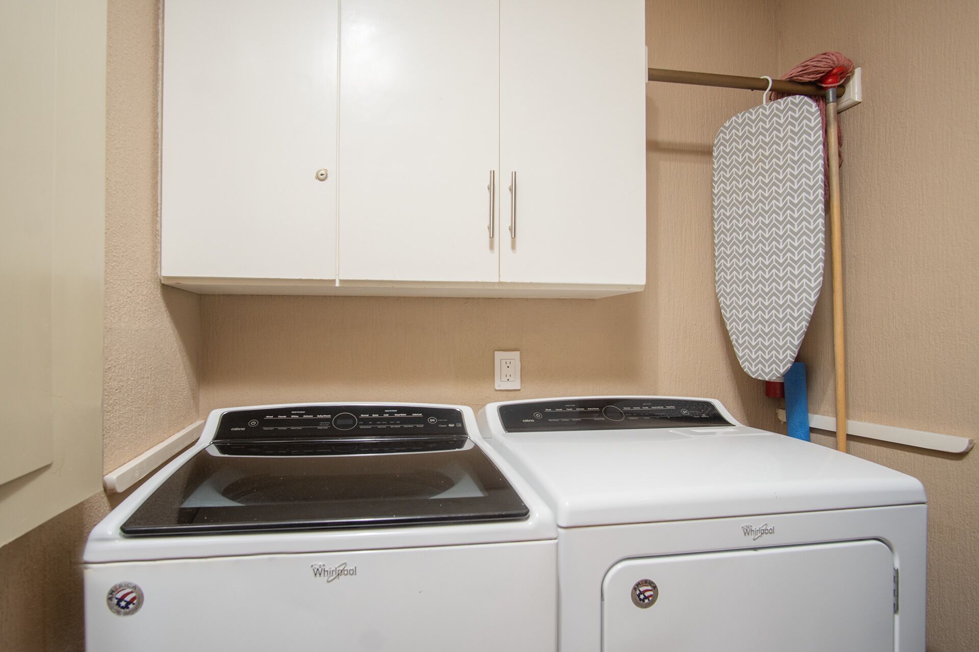 Uma área de lavandaria com duas máquinas de lavar Whirlpool e um armário branco acima.