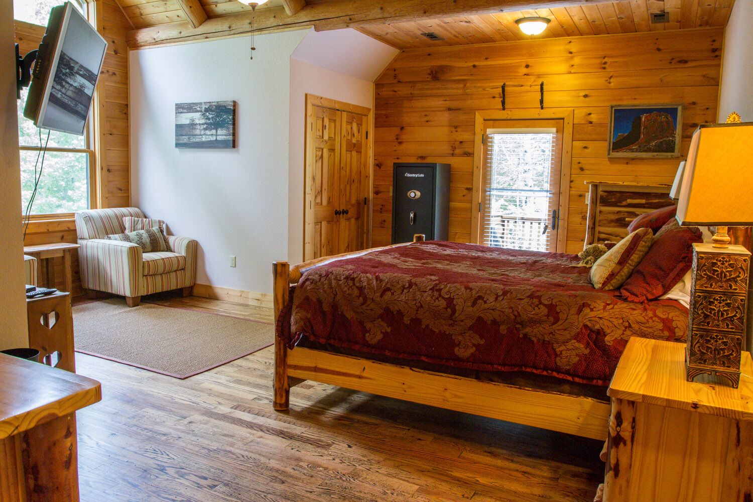 A wooden cabin bedroom with a bed, a TV, a chair, and a desk.